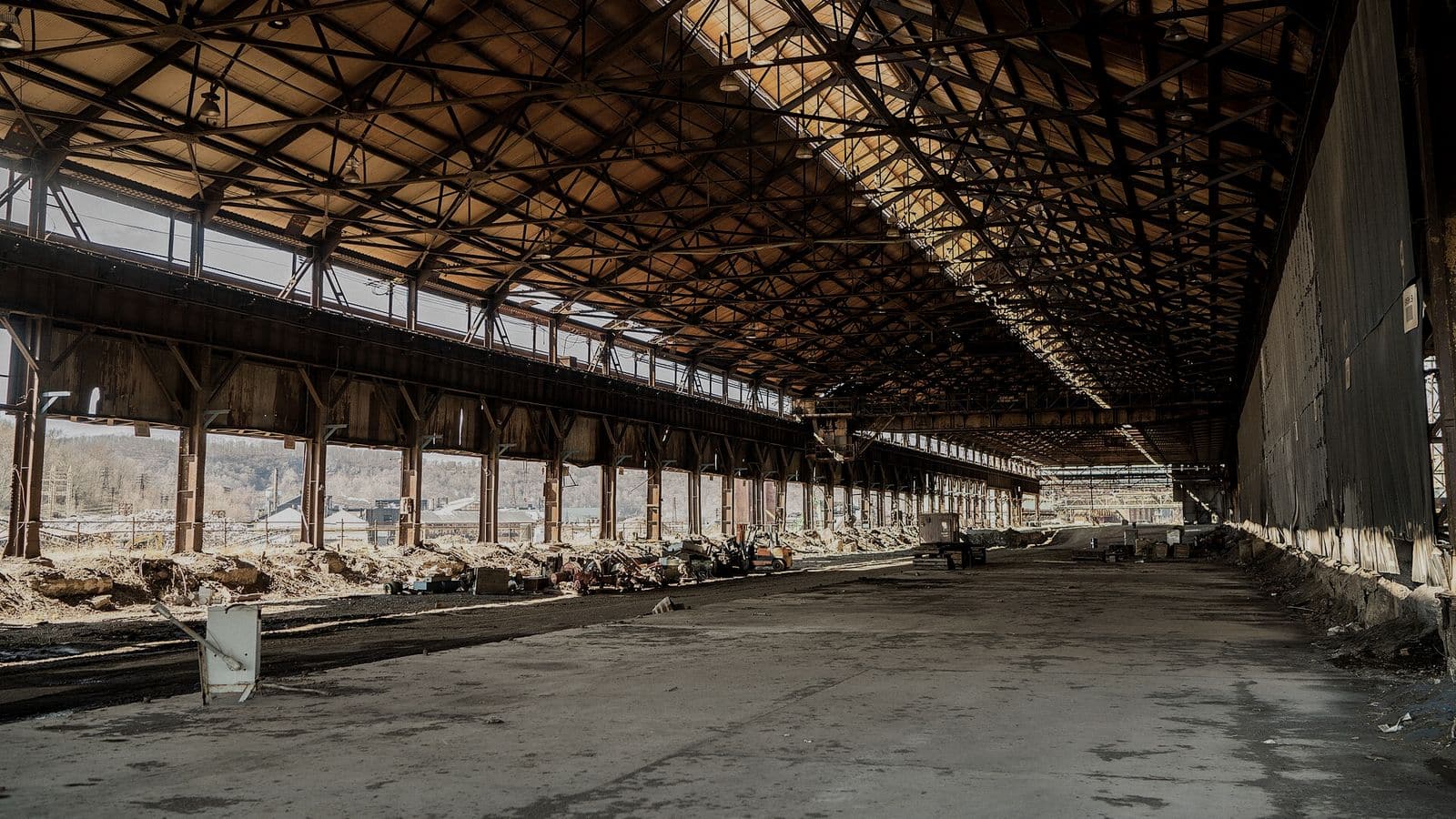 The stripped interior of a steel mill hall during dismantling, bare columns and a riveted truss roof over a swept floor